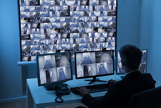 Man in control room watching surveillance footage from behind