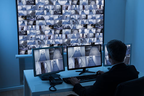 Rear View Of A Man In Control Room while Monitoring Multiple CCTV Footage