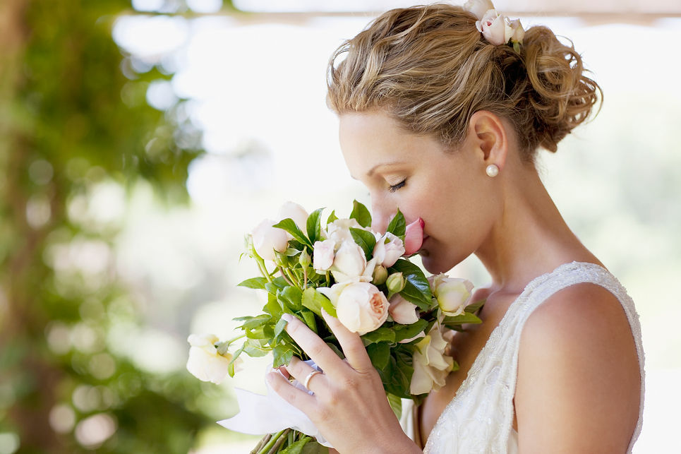 A bride with blonde hair in an elegant updo gently smells a bouquet of white and pink roses
