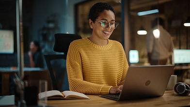 black woman with short hair in her office working on her laptop smiling