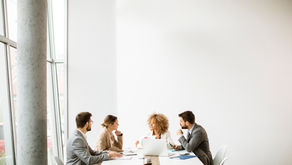 A small team engages in a focused meeting, exchanging ideas around a table in a bright, modern office space, aiming for efficient collaboration.