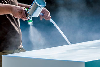 Hand holding a spray gun and painting wood in furniture factory