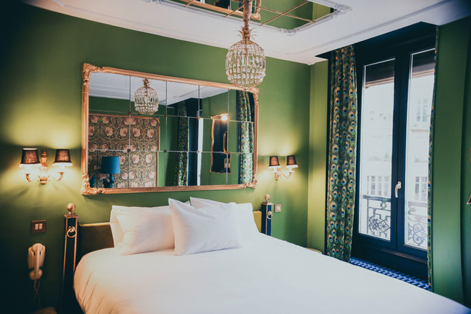 Green bedroom with bed, mirror, chandelier, and window; luxury hotel room.