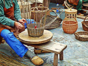Traditional basket weaver constructing a new basket with finished products in the background.