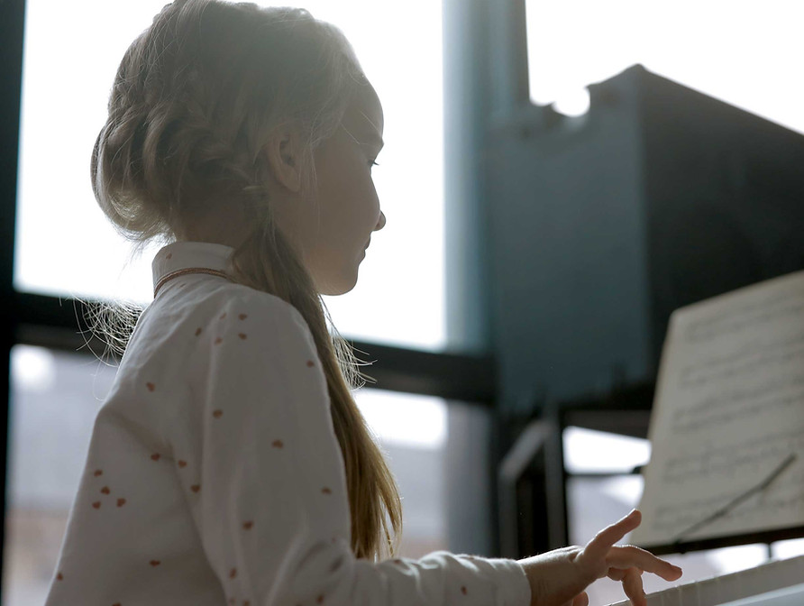 Child playing the piano, reading music.