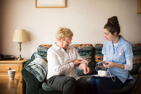 Healthcare professional performing a blood pressure health check during a home visit for a senior patient