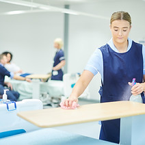 A worker in a blue apron cleans a table