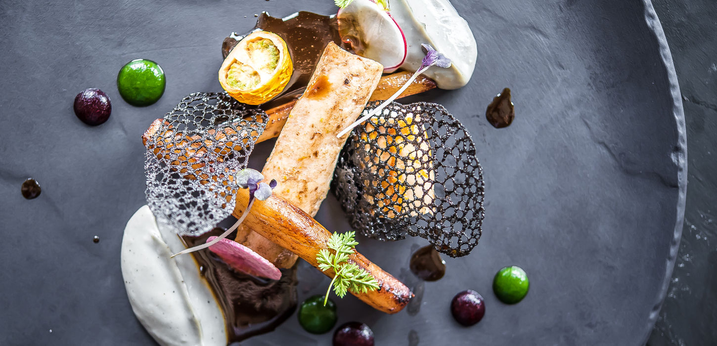 Gourmet plated dish with roasted vegetables and sauces.