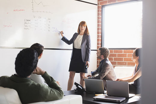 Woman presenting on a whiteboard to a seated business audience