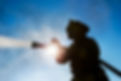 Fireman spraying fire photographed from low angle with the sun shining through. Horizontal