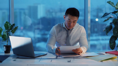 Office employee working late at a desk, illuminated by computer screen and overhead light, symbolizing overtime hours.