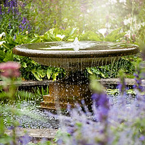 Beautiful summer garden with water fountain in amongst the flowers, in the hazy sunshine