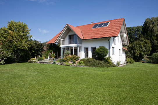 A house with red tiled roof, solar panels and a garden in front