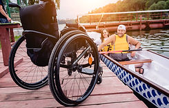 Male and female in a boat smiling with a wheelchair left behind on the dock