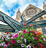 old fashioned signpost, with flowers planted in front of it, with signs pointing in multiple directions.