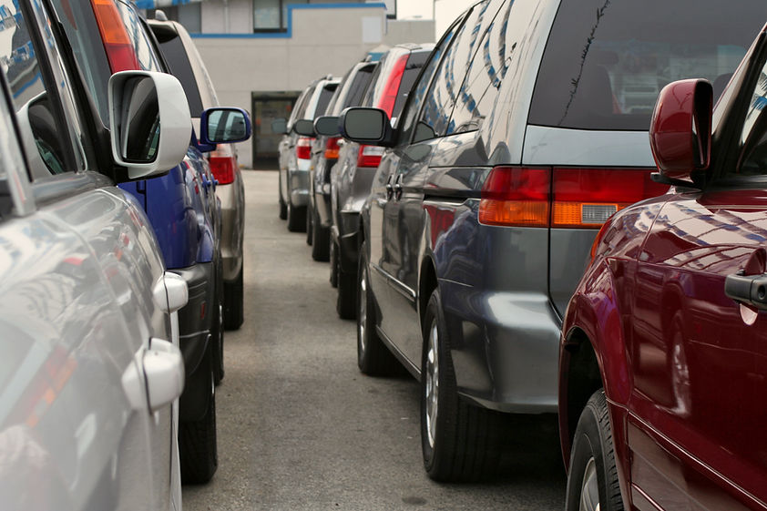 Row of used cars parked close together in a outdoor dealership lot with a focus on a red car in the foreground