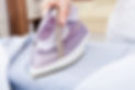 A person ironing a blue striped shirt with a modern purple steam iron on an ironing board
