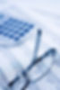 A pair of glasses and a calculator rest on financial spreadsheets filled with numbers