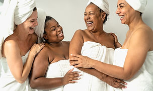 Women of colour wearing towels around their bodies and hair smiling and laughing with each other