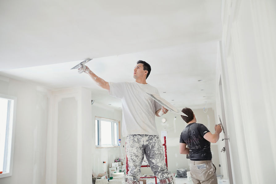 Two people applying plaster to walls in a room under renovation