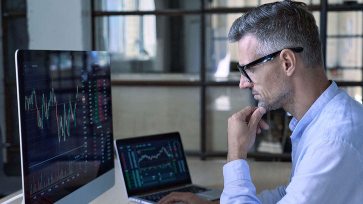 Analyste financier surveillant des graphiques boursiers sur plusieurs écrans