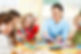 A teacher in a blue shirt joyfully interacts with children at a classroom table