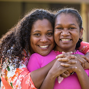 Mother and daughter of aboriginal descent smiling at camera and embracing each other