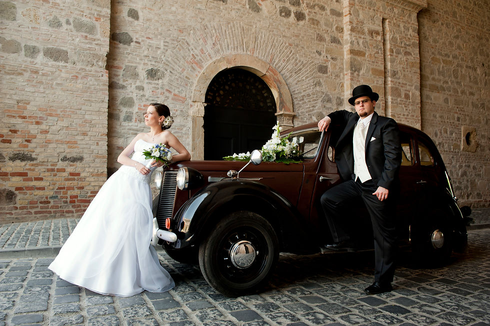 Bride and groom posing by classic vintage wedding car outside stone archway UK