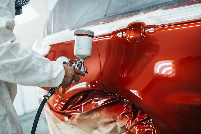 Man with protective clothes and mask painting car using spray compressor