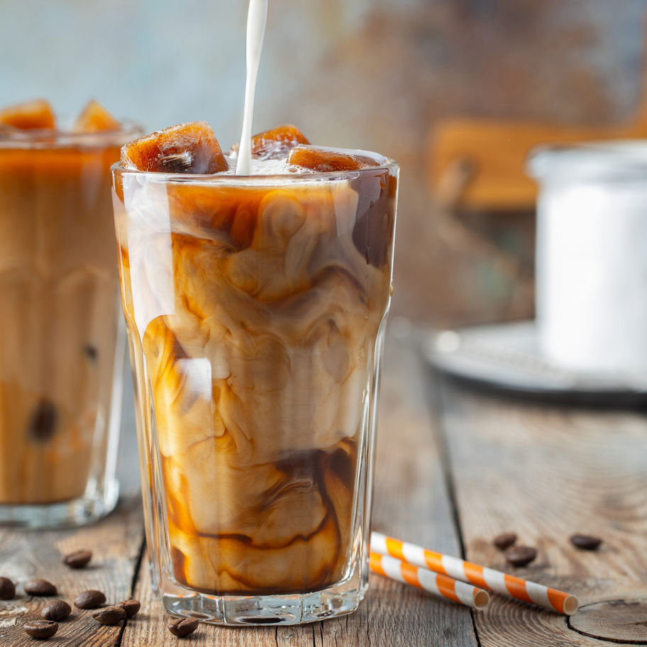 Pouring milk into ice coffee drink, hazelnut mocha, coffee beans and mug