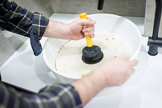 Hands holding a yellow-handled plunger in a white sink with water stained brownish