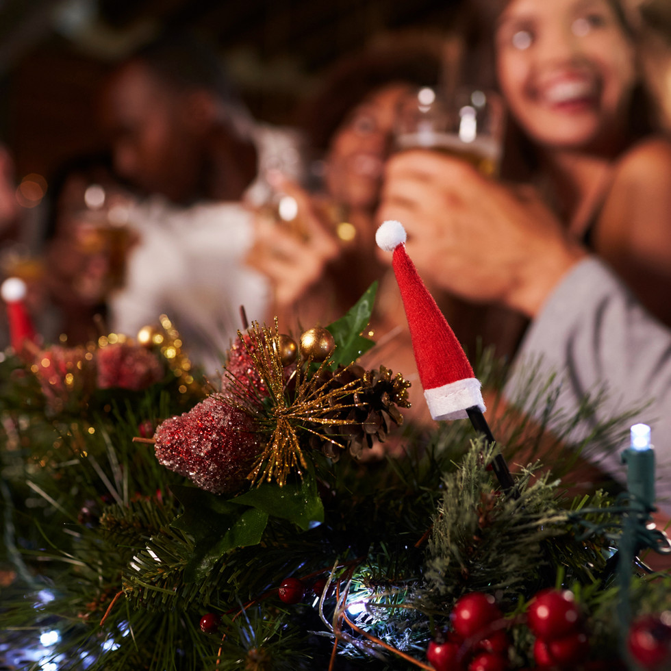 people eating and drinking around a table with Christmas garland in the front