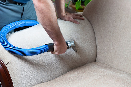 Close-up of a technician using a specialized vacuum tool to steam clean the armrest of a beige upholstered armchair