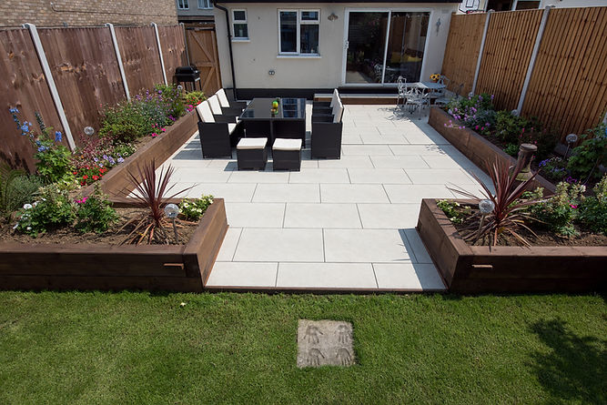 A patio with white porcelain slabs and wooden railway sleeper flowers beds
