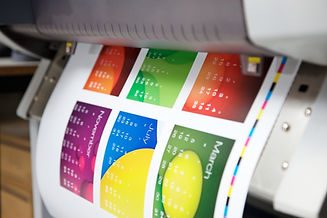 A printer dispenses a colorful page featuring multiple calendar designs with bold colors