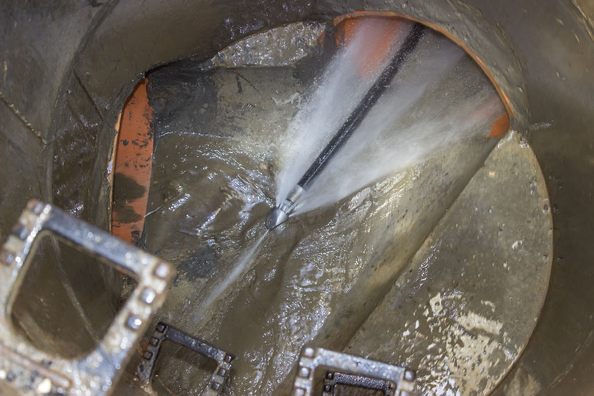 A high-pressure water jet cleans the inside of a large, muddy sewer pipe