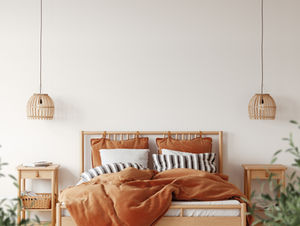 Cozy bedroom with a wooden bed, rust-colored bedding, striped pillows, and rattan lamps. White walls and plants create a calming vibe.