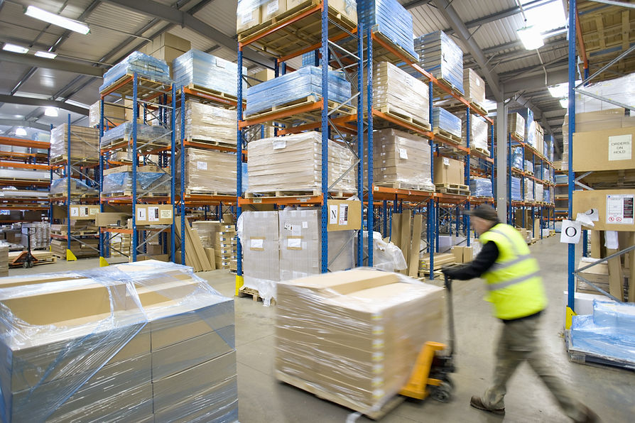 Warehouse worker pushing pallet truck with cardboard boxes