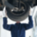 Mechanic working on car, face obscured by wheel, low angle view