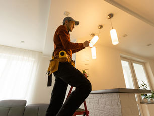 Electrician on a ladder fitting a ceiling light in a client's home — job scheduling software