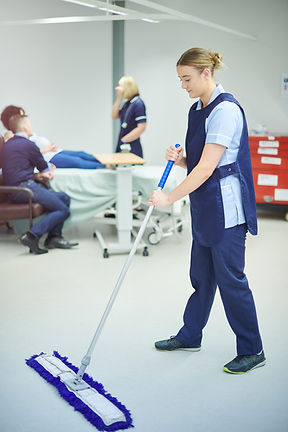 A person in blue pants uses a mop with a blue fringe to clean a light-colored floor.