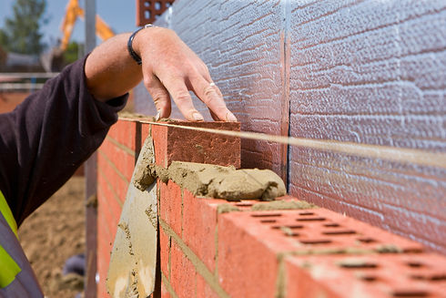 A close-up of a builder's hand laying red bricks with fresh mortar, using a string line for alignment