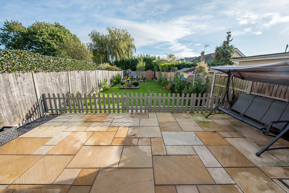 A patio featuring a wooden bench with a fence in the background, surrounded by greenery