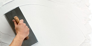 Plasterer applying smooth finish plaster coat to internal wall with trowel