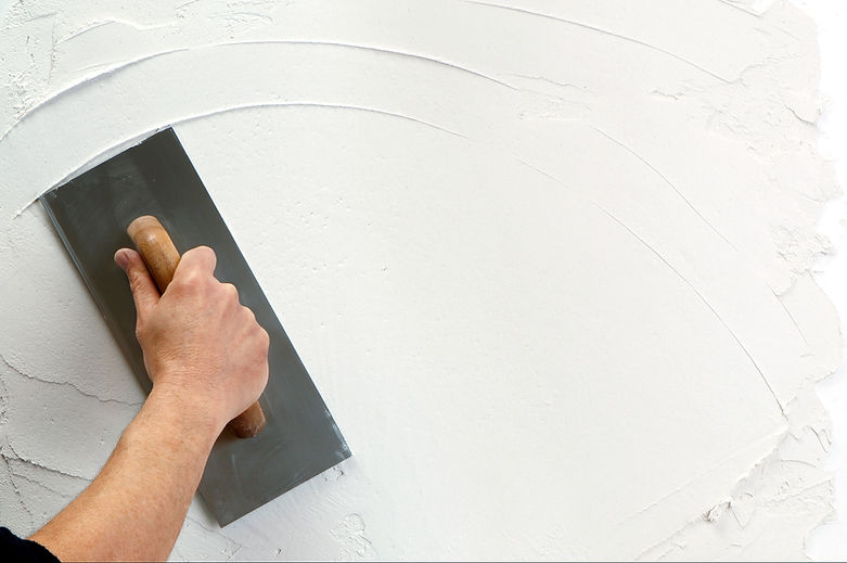 A hand uses a trowel to smoothly apply white plaster on a wall