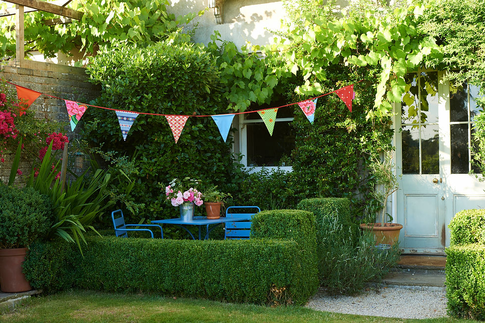 Leafy green garden with raised planter beds seating area and patio paths outside a house entry
