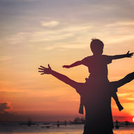 silhouette d'un père et de son fils qui tendent les bras face au coucher du soleil