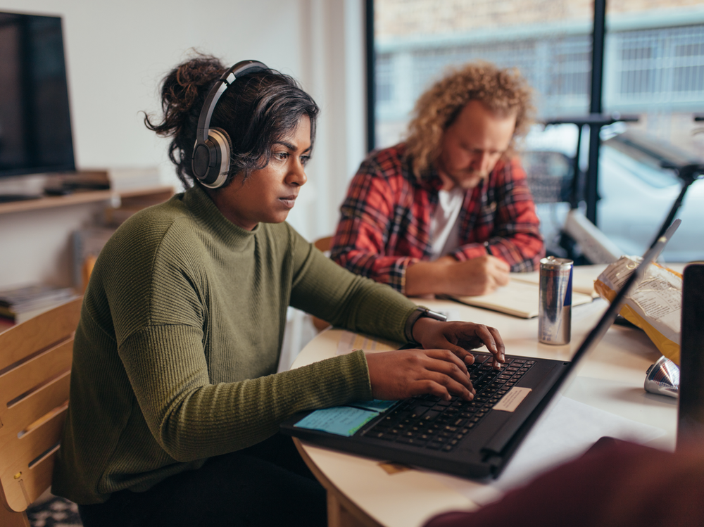 woman facing a laptop and to her left there is a man taking notes