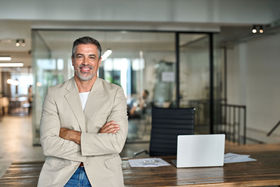 A successful business owner smiling, standing with arms crossed in a modern office.