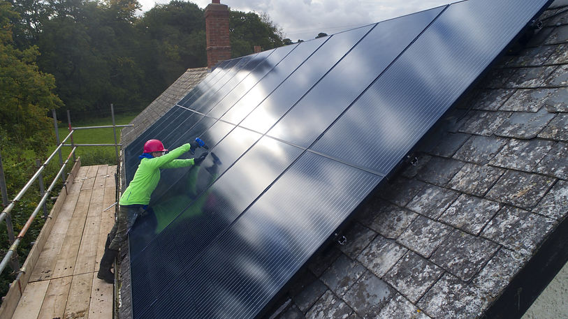Solar technician in high-vis clothing installing photovoltaic panels on a slate roof